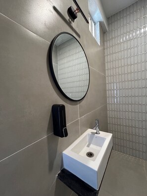 A bathroom with a white sink, a round mirror, and a soap dispenser on the wall.