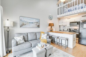 A modern living room with a grey sofa, a coffee table, and a kitchen area with a wooden island and bar stools.