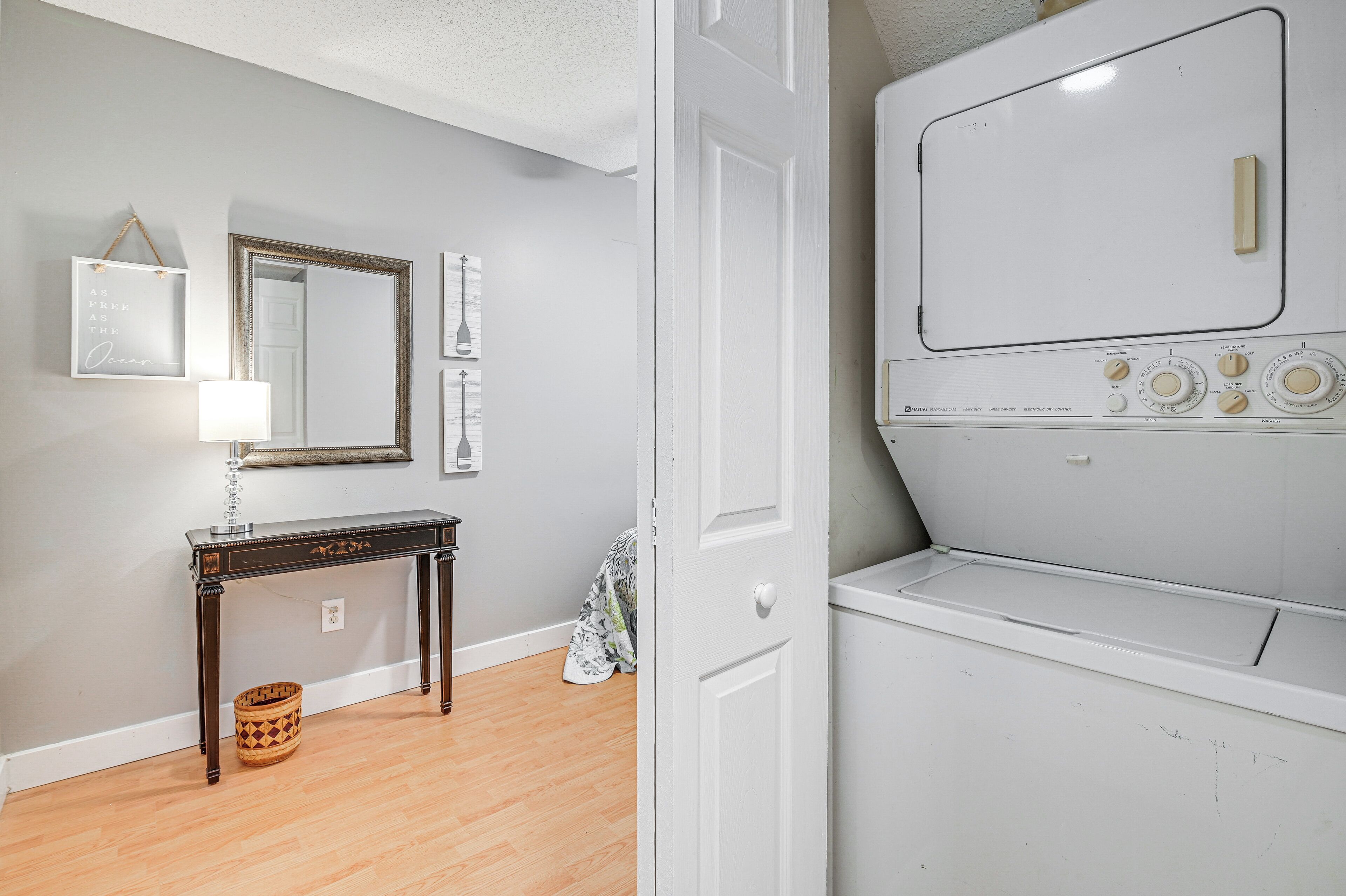 Une buanderie avec un lave-linge et un sèche-linge blancs, une console en bois surmontée d’une lampe et un miroir accroché au mur.