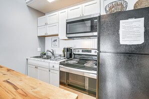 A modern kitchen with white cabinets, a stainless steel refrigerator, a microwave, a stove, and a sink.