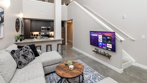 Een moderne woonkamer met een grijze hoekbank, een salontafel en een flatscreen televisie aan de muur.
