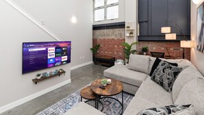Een moderne woonkamer met een flatscreen televisie, een grijze bank, een salontafel en een metselwerk muur.
