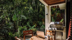 A patio with a wooden table, chairs, and a laptop. There is a grill and lush greenery in the background. - Villa del BroDor Amor, beautiful home with access to 2 beaches Tamarindo and Langosta (Playa Langosta)