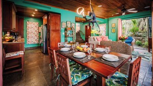 A dining area with a wooden table set for four, a kitchen in the background, and a ceiling fan. - Villa del BroDor Amor, beautiful home with access to 2 beaches Tamarindo and Langosta (Playa Langosta)