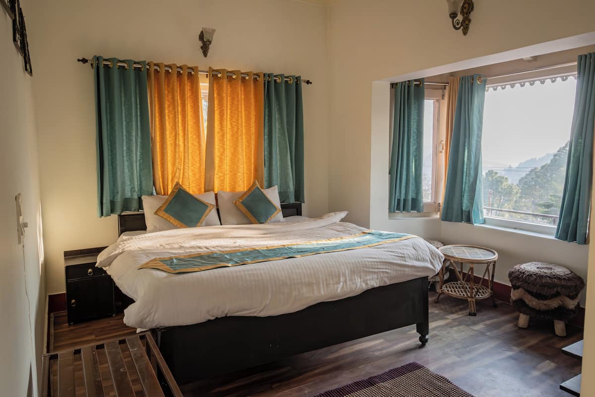 A bedroom with a bed, nightstands, a window with curtains, a small round table, and a stool.