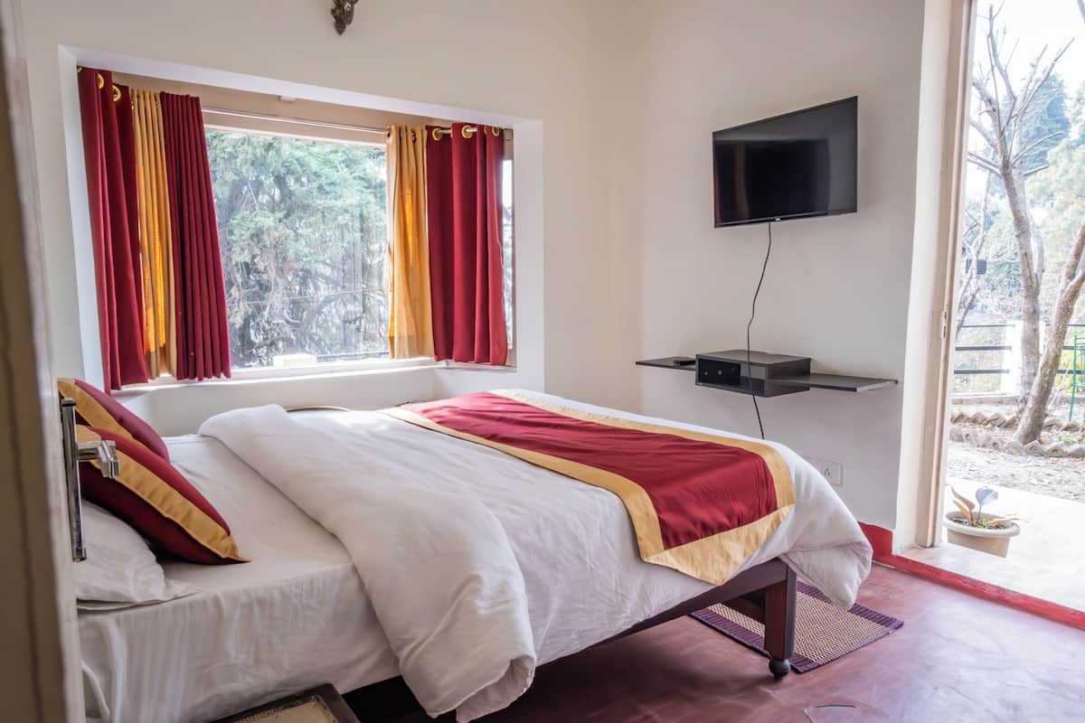A hotel room with a bed, a TV mounted on the wall, and a window with curtains.