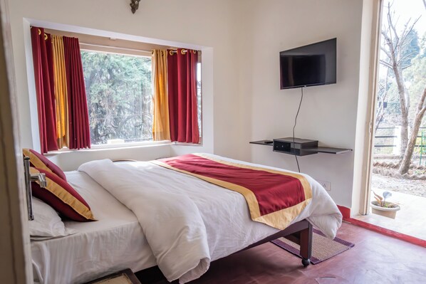 A hotel room with a bed, a TV mounted on the wall, and a window with curtains. - Dew Drops Homestay (Nainital)