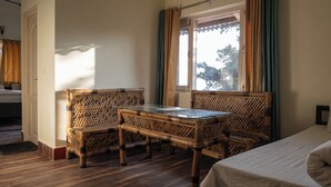 A room with a bed, a glass-top table, two wicker chairs, and a window with curtains.