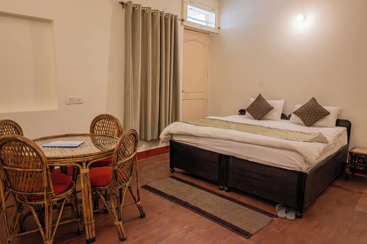 A bedroom with a bed, a table with chairs, a window, and a door.