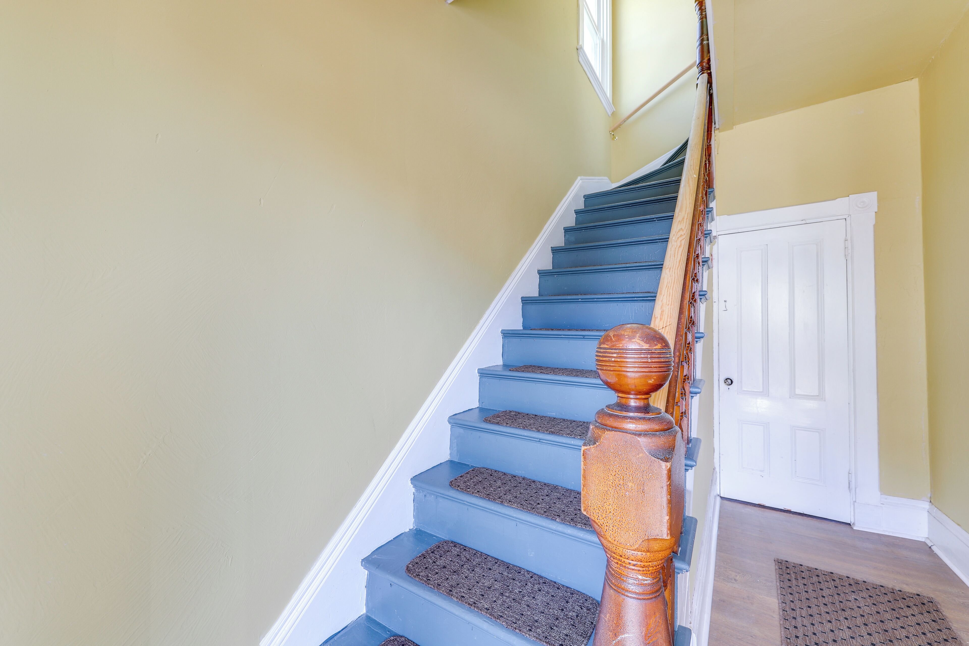 Eine Treppe mit blauen Stufen und einem hölzernen Geländer, die zu einer weißen Tür führt.