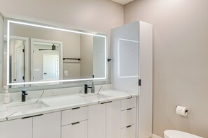 A modern bathroom with a large mirror, two sinks, and a toilet.