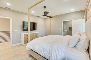 A modern bedroom with a large bed, a ceiling fan, a TV mounted on the wall, and a wooden floor.