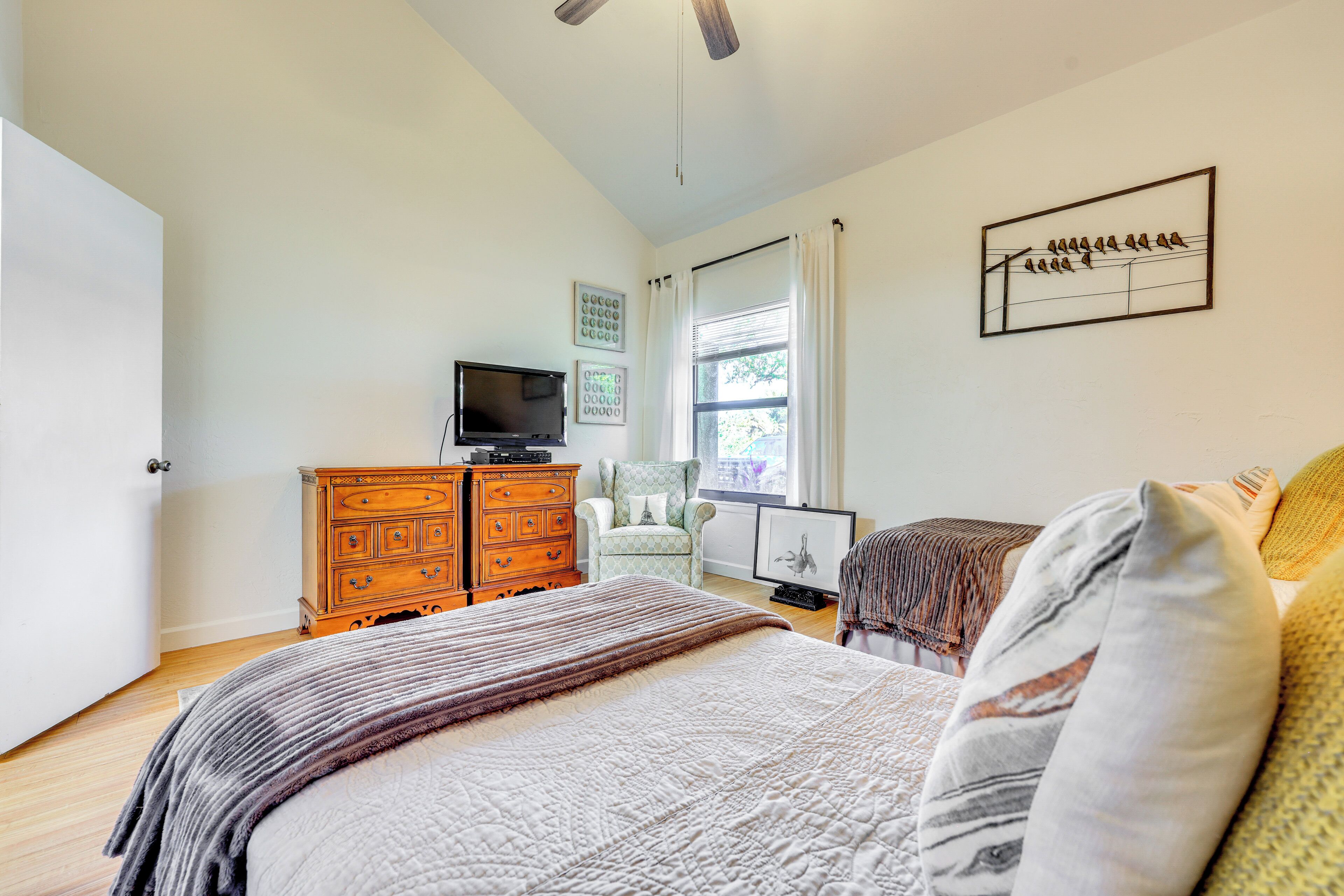 A bedroom with a bed, a dresser, a chair, a television, and a window with curtains.