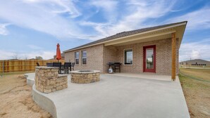 Una casa con un patio que incluye un brasero, asientos exteriores y un porche cubierto.
