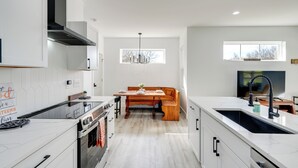Een moderne keuken met witte kasten, een inbouwoven, een eethoek met een houten bank en een groot raam dat natuurlijk licht biedt.