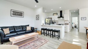 Een moderne woonkamer met een zwarte leren bank, een houten salontafel en een keuken met witte kasten en zwarte krukken.