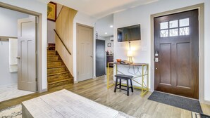 Un vaste espace de vie agrémenté d’un escalier en bois, d’une table à manger avec un banc, d’un téléviseur fixé au mur et d’une porte en bois foncé.
