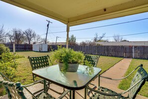 A covered patio with a glass table and metal chairs, surrounded by a wooden fence and a grassy yard. - Family Friendly: Peaceful Home in Stamford! (Stamford)