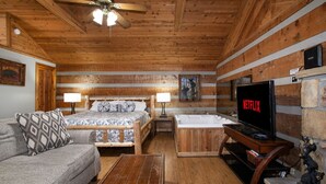 Ein Holzblockbau-Innenraum mit einem Bett, einer Couch, einem Fernseher und einem Kamin.