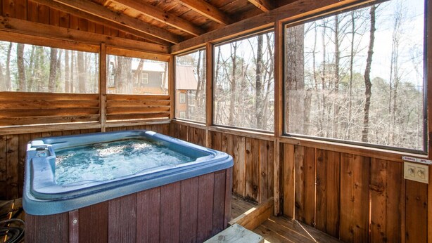 Eine Holzhütte mit Whirlpool, großen Fenstern und Blick auf den Wald.