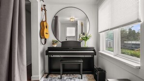 A piano, a bench, a guitar, a mirror, and a window with a view of the outside. - Bluebird | Charming 3-Bedroom Home in Drumheller! (Drumheller)