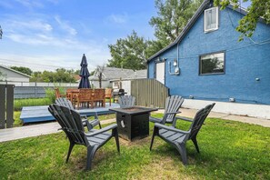 Un jardin avec une table et des chaises de patio, un foyer extérieur et une maison bleue.