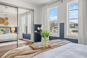 Une chambre à coucher avec un lit, une table de chevet avec une lampe, une fenêtre avec des rideaux et un miroir qui reflète la pièce.