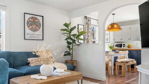 A modern living room with a blue sofa, a wooden coffee table, and a large plant. - Bluebird | Charming 3-Bedroom Home in Drumheller! (Drumheller)