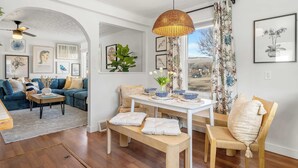 A living room with a sofa, a dining table with chairs, a bench, and a hanging light fixture. - Bluebird | Charming 3-Bedroom Home in Drumheller! (Drumheller)