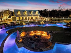 Une maison avec une piscine, un foyer extérieur et une terrasse bien éclairée.