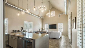 Une cuisine spacieuse dotée d’un grand îlot central, de luminaires suspendus et d’un parquet en bois disposé en chevrons.