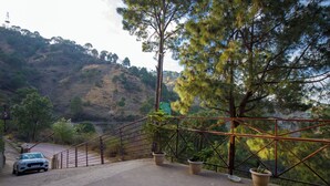 A paved area with a car parked on the left, a metal railing, and potted plants. - Alaya Stays Captains Nest 3 BHK Retreat With Garden & Scenic Views (Kasauli)