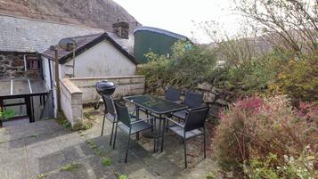 A patio with a table and chairs, a barbecue grill, and a stone wall.