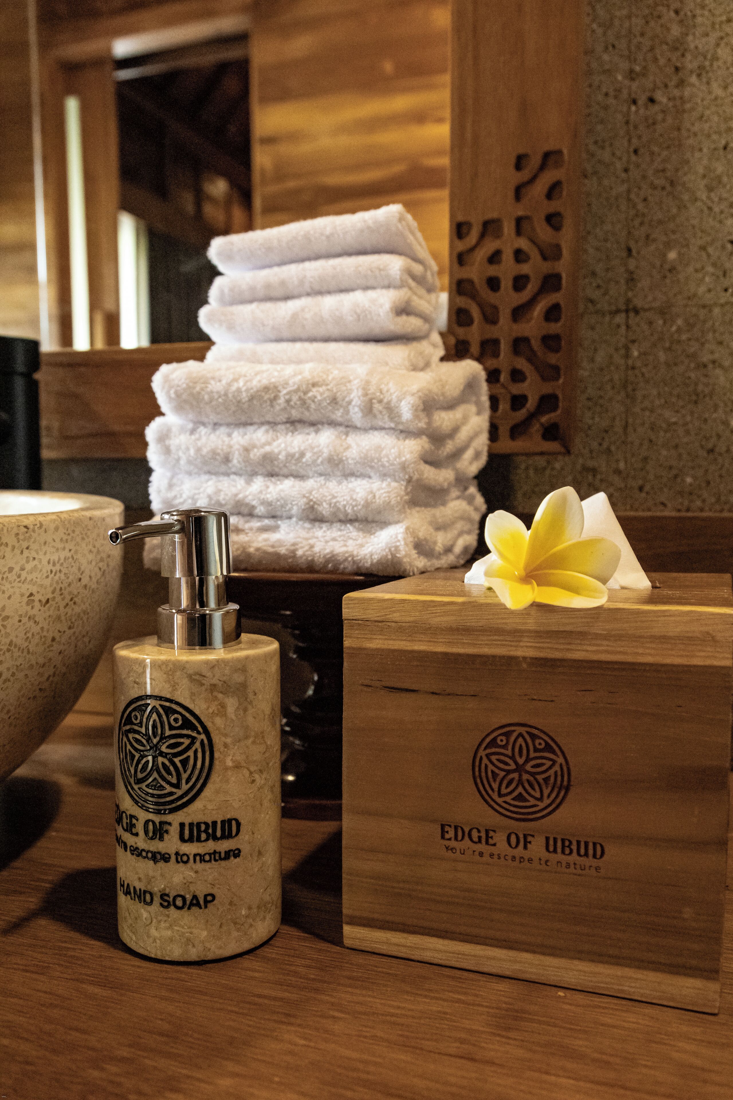 A wooden counter with a hand soap dispenser, a bowl, and a stack of towels.