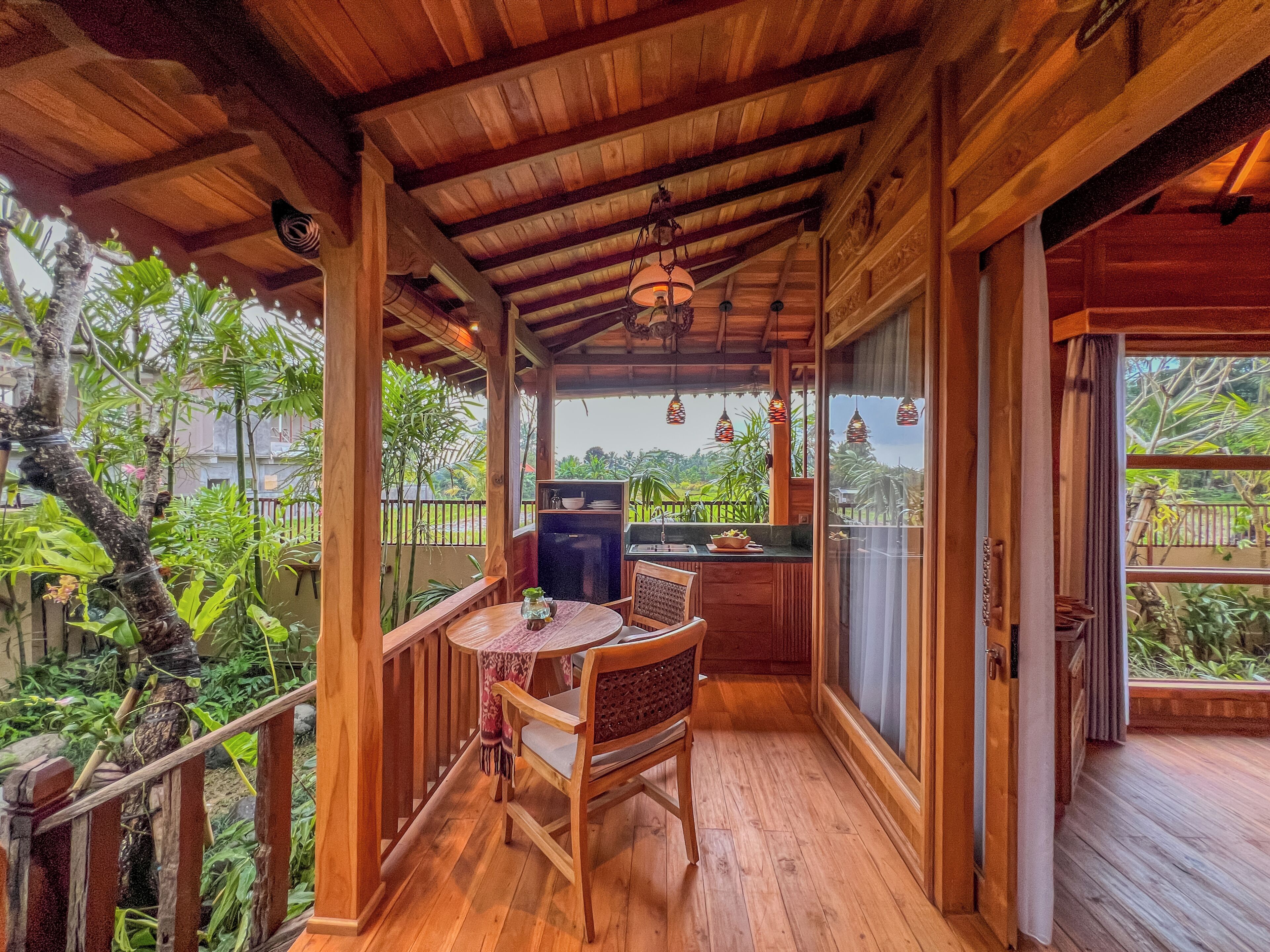 Una terraza de madera con mesa y sillas, un refrigerador y vista a follaje.