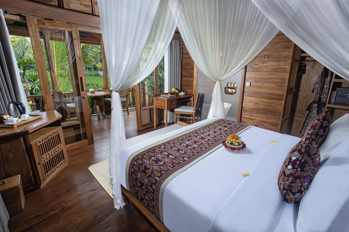 Une chambre avec un grand lit, un bureau et une chaise, donnant sur un paysage verdoyant.