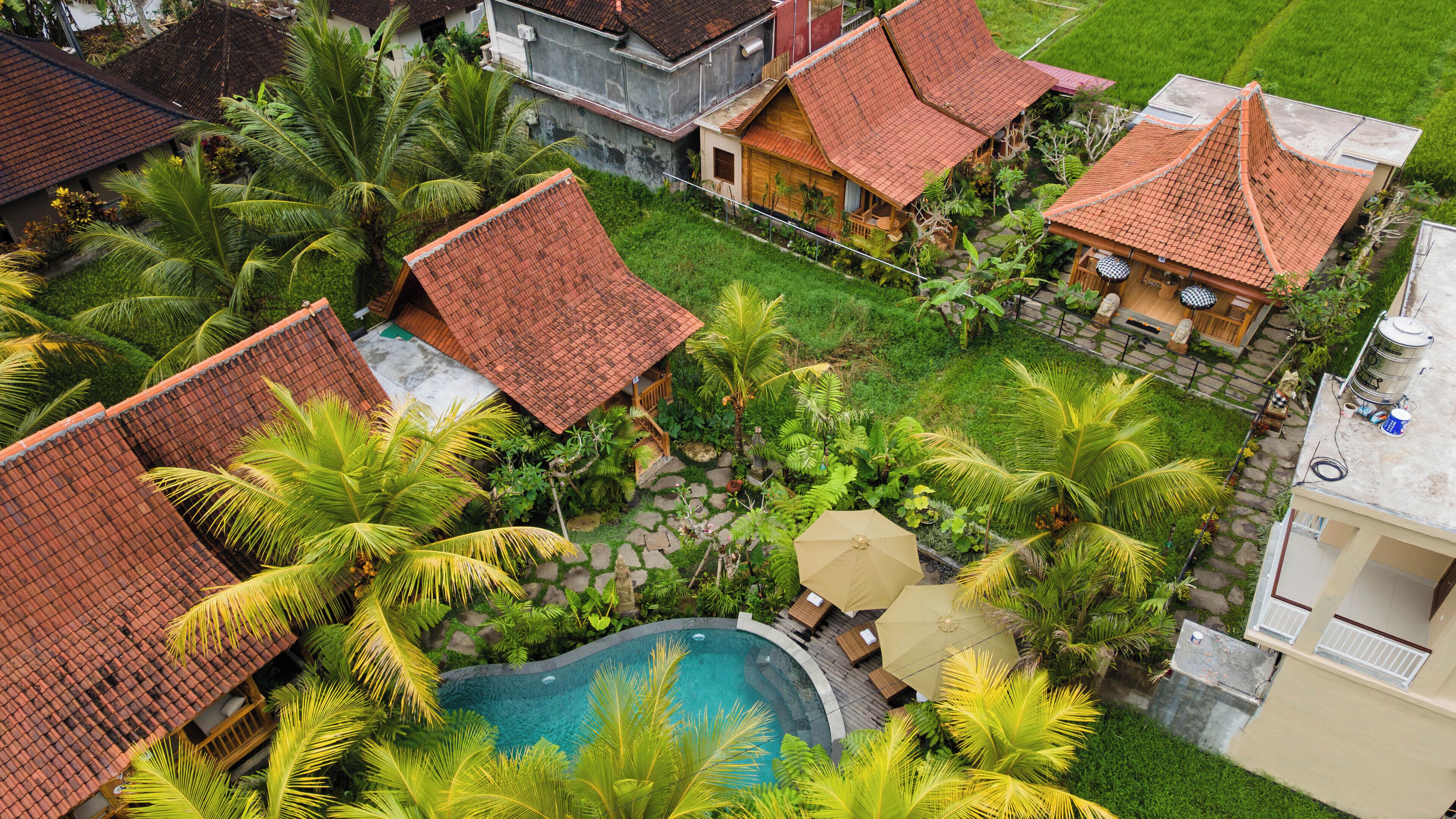 A residential area with a swimming pool surrounded by lush greenery and houses with red-tiled roofs.