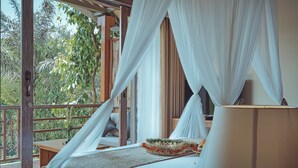 Un dormitorio con una cama, una mesita de noche, una lámpara y vistas al exterior con vegetación.