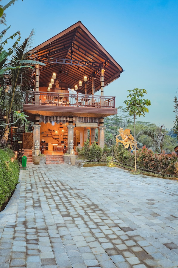 A two-story building with a wooden balcony and a large sculpture in the garden. - Harsa Sanctuary (Sebatu)