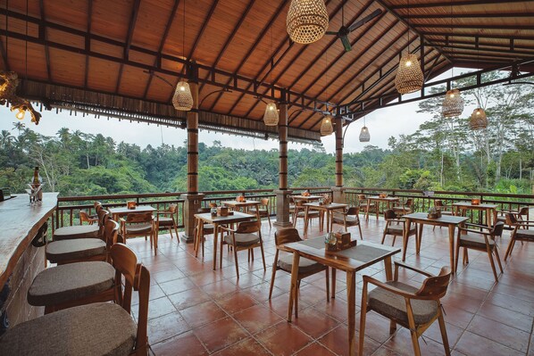 An outdoor dining area with wooden tables and chairs, surrounded by a wooden pergola with hanging lights, overlooking a lush green landscape. - Harsa Sanctuary by GenuineHost (Sebatu)