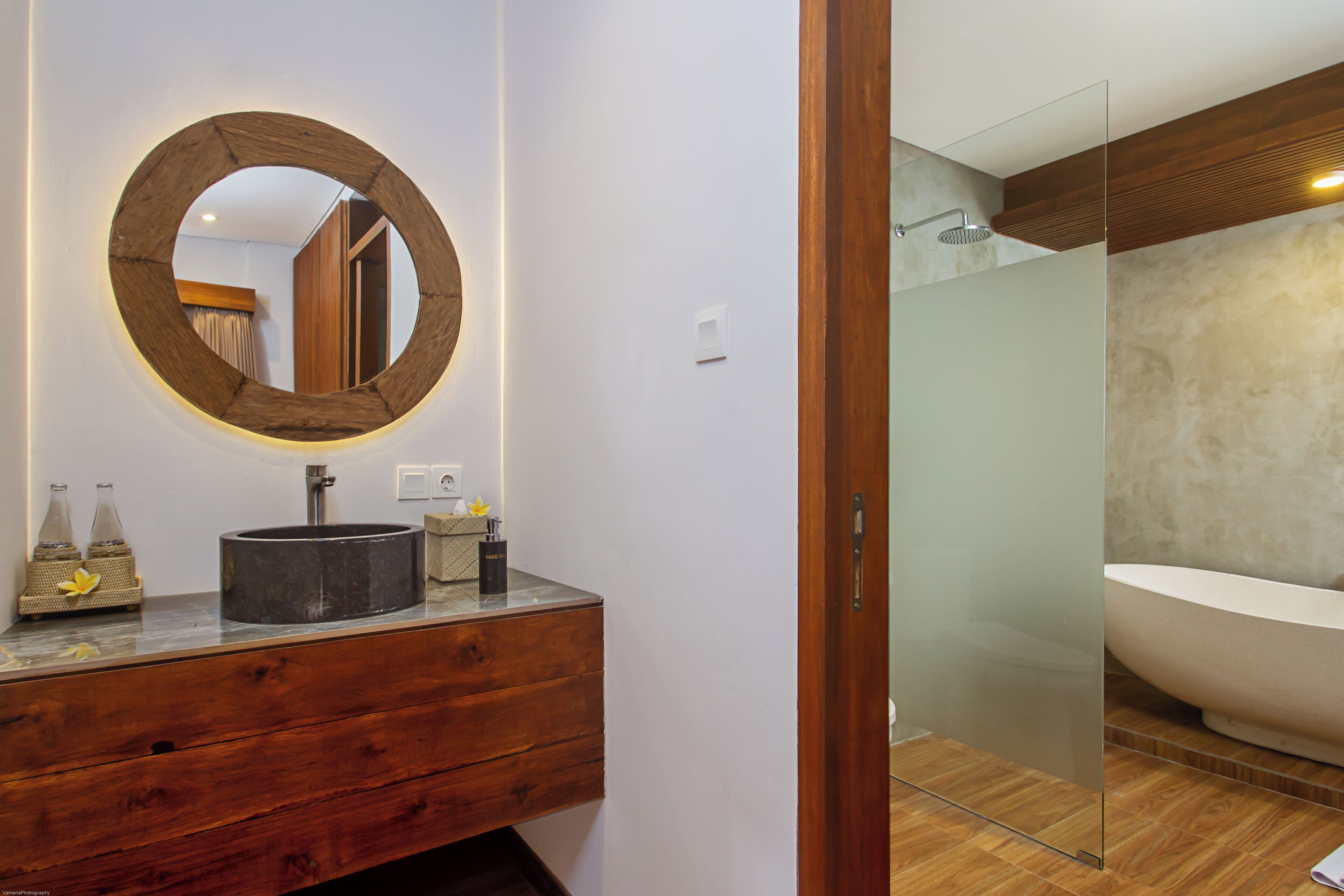 Ein modernes Badezimmer mit einem Holz-Waschtisch, einem runden Spiegel und einer großen Badewanne.