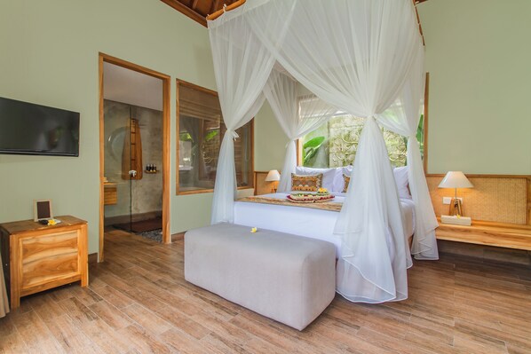 A bedroom with a canopy bed, a bedside table, a bench, a TV, and a glass door leading to a bathroom. -  Reswaha Villas by GenuineHost (Ubud)