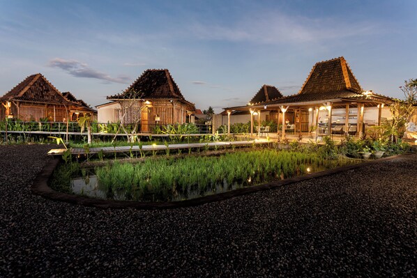 A traditional wooden building with a thatched roof, surrounded by a garden with a small pond and gravel paths. - DITUJU Ubud by GenuineHost (Sukawati)