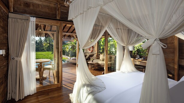 A bedroom with a canopy bed, wooden walls, and a view of an outdoor seating area.