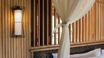 A room with a bed, a nightstand, a wall-mounted lamp, and a window with vertical wooden slats.