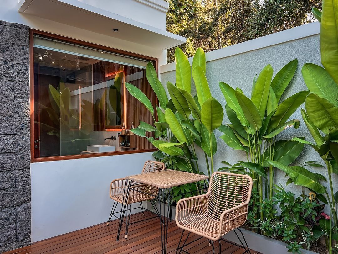 Un patio con piso de madera, mobiliario de mimbre y plantas verdes grandes.