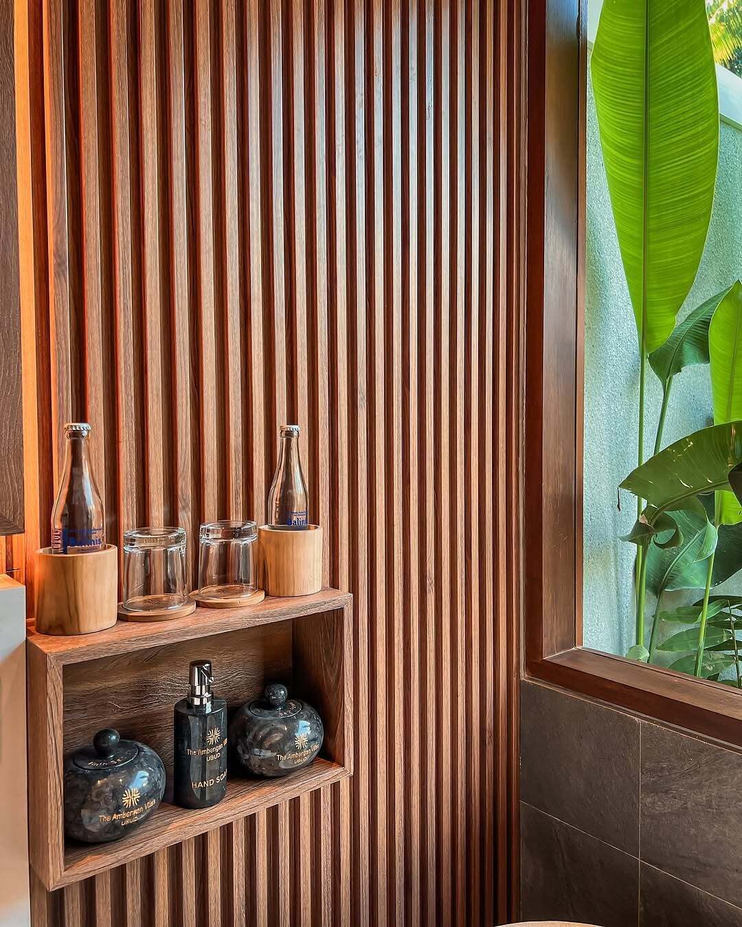 Une étagère en bois, ornée de verres et d’un objet décoratif, est adossée à un panneau mural vertical en bois.