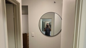 Un couloir avec un grand miroir rond accroché au mur, un plancher en bois et une porte donnant sur une autre pièce.