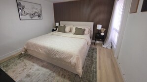 A bedroom with a bed, a ceiling fan, a nightstand with a lamp, and a window with blinds.