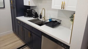 A modern kitchen with a black and white color scheme, featuring a coffee maker, sink, and a dish rack.